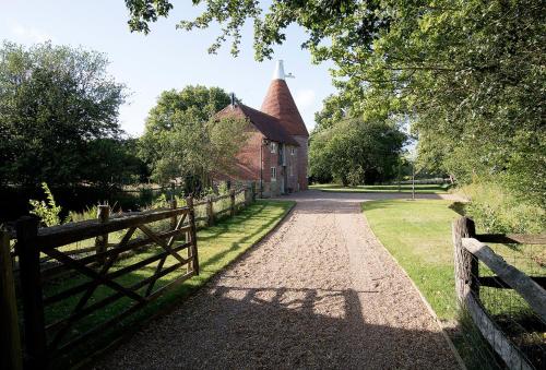 an old building with a fence and a church at Bakers Farm Oast in Ticehurst