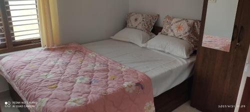 Cama pequeña con edredón y almohadas rosas en Kailash Guest Home en Mysore