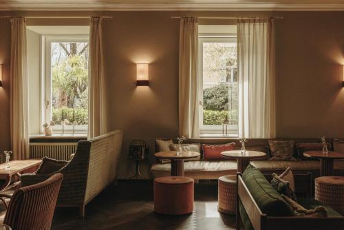 a restaurant with couches and tables and windows at Parkhotel Mondschein, a Member of Design Hotels in Bolzano