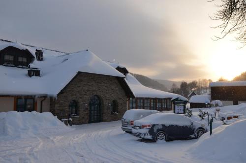 a house covered in snow with cars parked in the driveway at Landhotel Rittersgrün in Breitenbrunn