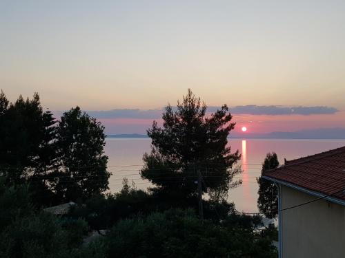a sunset over the water with trees and a house at Levante Breeze in Xirokástellon