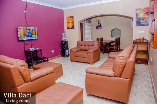 a living room with brown leather furniture and a dining room at Villa Daci in Gulu