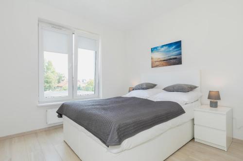 a white bedroom with a bed and a window at Jantar Apartament Pogodne in Kołobrzeg