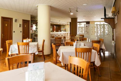 Hotel América Ferrol في فيرول: مطعم بطاولات بيضاء وكراسي خشبية