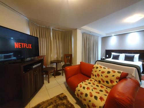 um quarto de hotel com uma cama, uma televisão e um sofá em Pousada Cheverny - Fácil acesso ao centrinho e Baden Bar em Campos do Jordão
