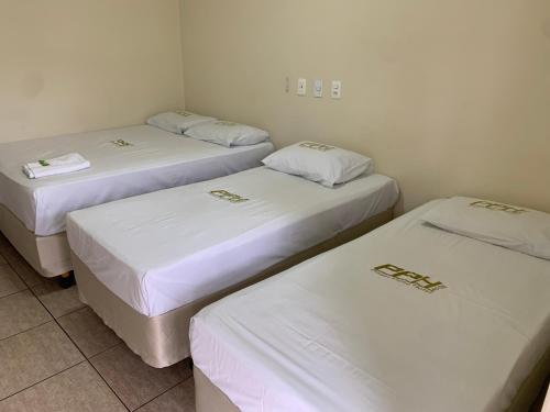 three beds in a room with white sheets at Pissin Plaza Hotel in Goiânia
