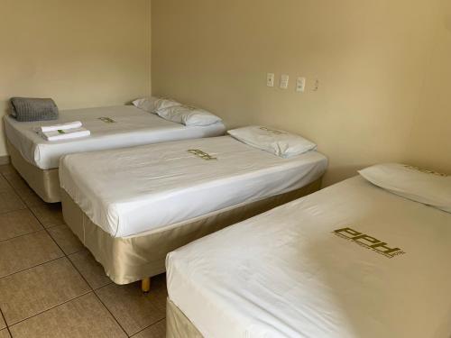 three beds in a room with white sheets at Pissin Plaza Hotel in Goiânia