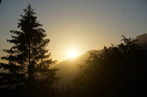 a sun setting over a mountain with trees in the foreground at HERZLI-CHALET über dem Rheintal mit Schlossblick in Werdenberg