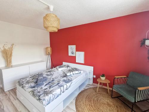 una camera da letto con una parete rossa, un letto e una sedia di Le Théâtre du Vieux Foyal - Appartement 4 personnes à Fort-De- France a Fort-de-France