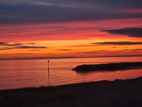 a sunset over a body of water with a beach at Awave From It All - Escape the city life in Jaywick Sands