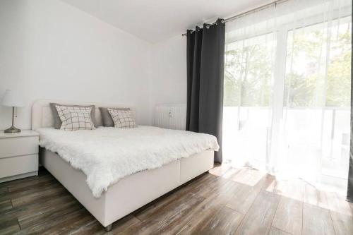 a white bedroom with a bed and a large window at ALURE RESIDENCES 1 & 24h self check-in in Banská Bystrica