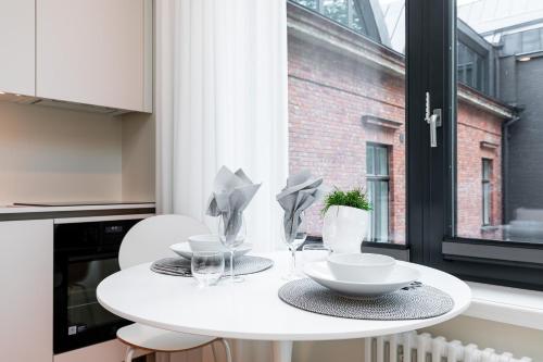 een witte tafel met borden en glazen en een raam bij Vallikraavi Cozy Apartment in Tartu