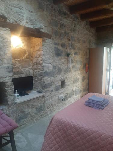 - une chambre avec un lit et une télévision dans un mur en pierre dans l'établissement Eleni's Cottage, à Apsiou