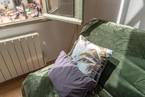 a green couch with a pillow and a window at Un pied à terre avec terrasse à la Cathédrale - Une Nuit à Nîmes in Nîmes