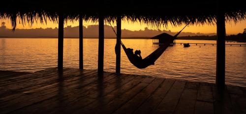 a person laying in a hammock on a dock near the water at Casa Cayuco Eco-Adventure Lodge in Bocas del Toro
