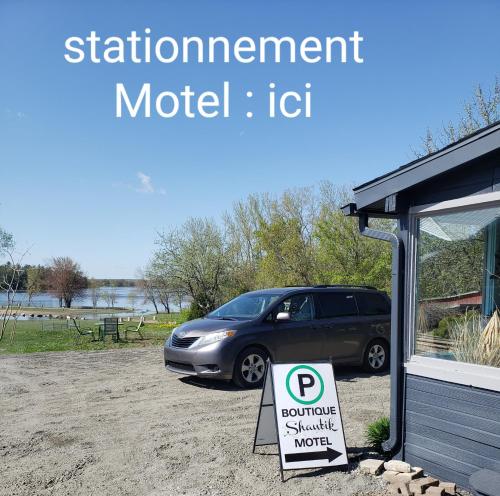 une voiture garée à côté d'un panneau devant un bâtiment dans l'établissement Motel Shantik, à Montebello