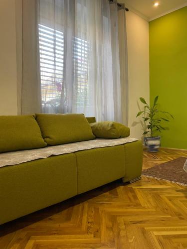 a green couch in a living room with a window at IGNIM 2 Apartment in Subotica