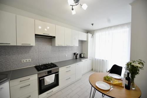 a kitchen with white cabinets and a wooden table at Cozy apartment next to the park in Ternopilʼ