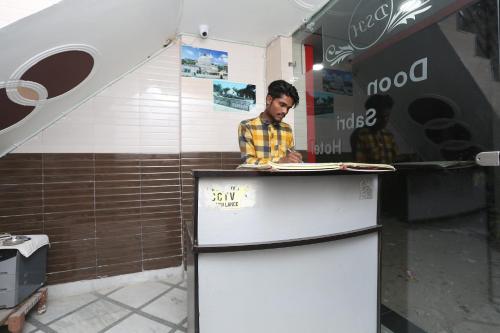 um homem atrás de um balcão com um frigorífico em SPOT ON Hotel Doon Sabri em Roorkee