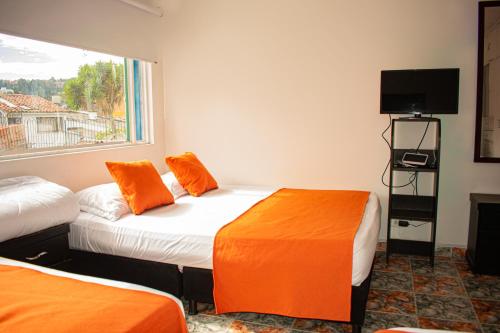 a room with two beds with orange pillows and a window at Hotel BogoSuba 127 in Bogotá