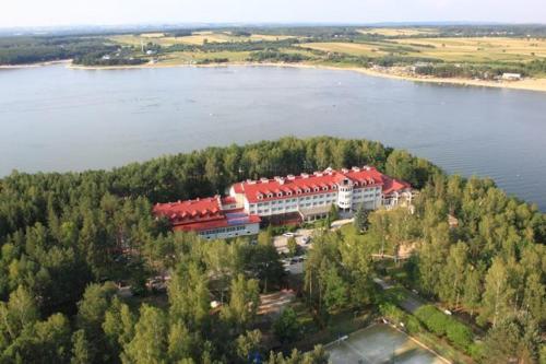 a large building with a red roof on a lake at Cztery Wiatry Aparthotel in Korytnica