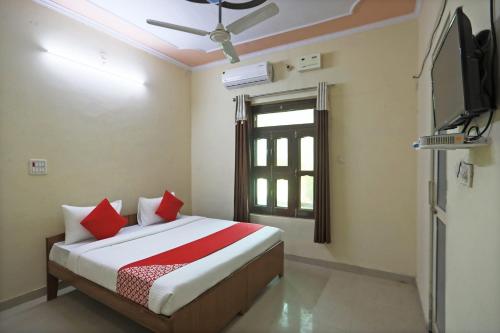 OYO 62761 Hotel Daksh في Mahendragarh: غرفة نوم بسرير ومخدات حمراء وتلفزيون