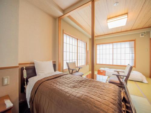 a bedroom with a bed and two chairs and two windows at Ryokan Hakura in Yamanouchi