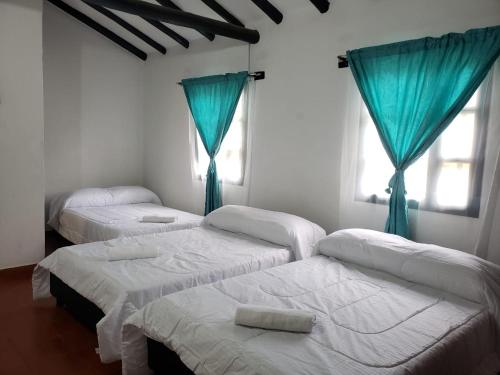 three beds in a room with blue curtains at Casa Villa Ramos in Villa de Leyva