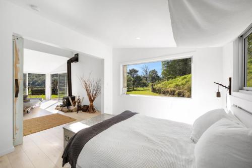 Dormitorio blanco con cama y ventana grande en Molla Eco Lodge, en Wattamolla