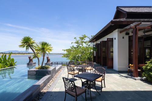 a patio with tables and chairs next to the water at Nghê Prana Hotel and Spa Hoi An in Hoi An