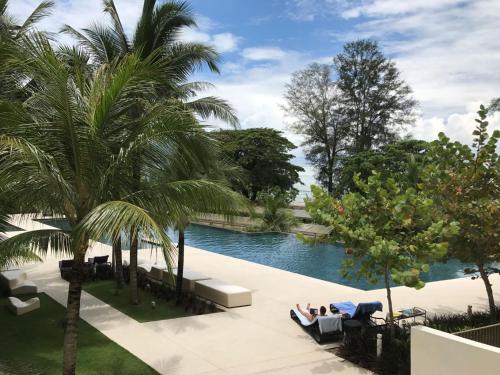 - une piscine avec des palmiers et des personnes assises sur un canapé dans l'établissement By The Sea - UBTS SMART ENTERPRISE, à Batu Ferringhi