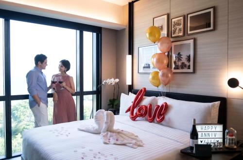 a man and a woman standing in a bedroom with a bed at The Outpost Hotel Sentosa by Far East Hospitality in Singapore
