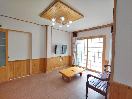 a room with a bench and a table and a tv at Gyulhouse Pension in Seogwipo