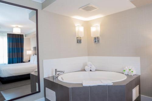 a bathroom with a tub and a bed and a mirror at Sandman Hotel Oakville in Oakville