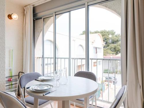 une table et des chaises blanches devant une grande fenêtre dans l'établissement Appartement à Gruissan avec Piscine - 4 Pers. - FR-1-409A-8, à Narbonne