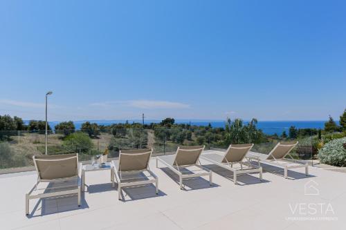 a row of chairs on a patio with the ocean in the background at Olive Grove Suites - Villas with private pool and garden in Nikiti