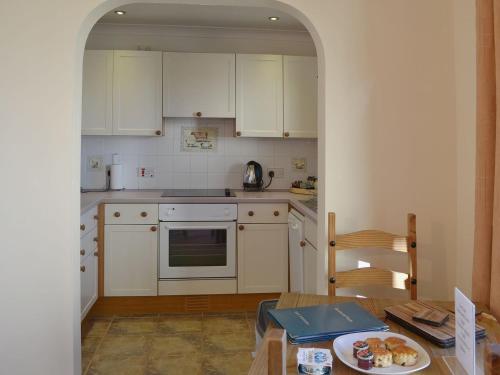 a kitchen with white cabinets and a table with a plate of food at Oaktree Cottage in Stoke Gabriel