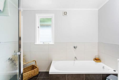 a white bathroom with a tub and a window at Spacious Family Retreat in City - Netflix - WiFi in Auckland