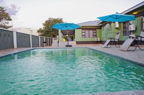 a swimming pool with blue umbrellas and a house at Amariah Lodge in Kasane