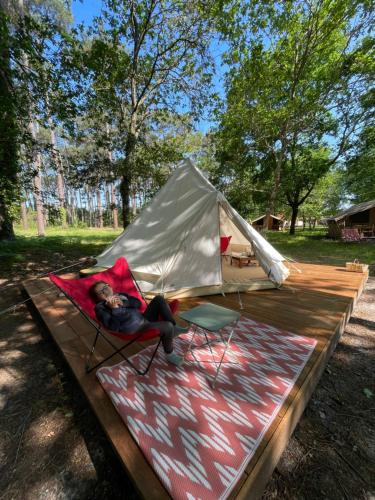 eine Person, die auf einem Stuhl neben einem Zelt liegt in der Unterkunft Tente Indiana Chênes - La Téouleyre in Saint-Julien-en-Born