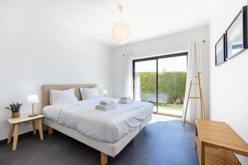 a white bedroom with a bed and a large window at Villa Botelha in Sagres