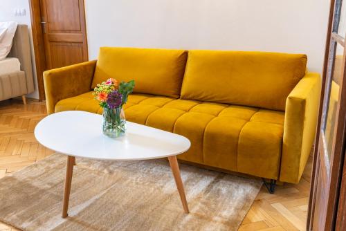 a yellow couch with a vase of flowers on a table at Primavera - Castle view apartments in Prague