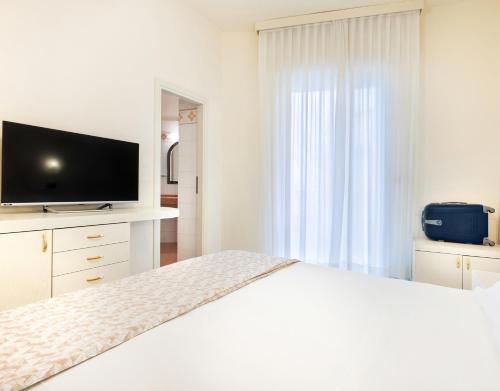 a white bedroom with a large bed with a flat screen tv at Hotel Fenice Gluten Free in Milano Marittima