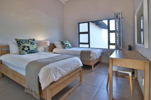 a bedroom with two beds and a desk and a window at Shorebreak in Southbroom