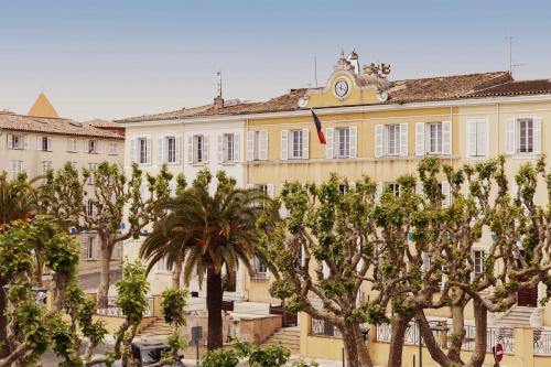 un grand bâtiment jaune avec des arbres devant lui dans l'établissement Coq Hotel, à Cogolin