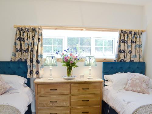 a bedroom with two beds and a vase of flowers on a dresser at Paterson Cottage in Tore