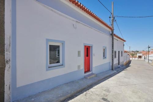 um edifício branco com uma porta vermelha numa rua em Rustic & Aesthetic House in Alqueva with Pool em Granja