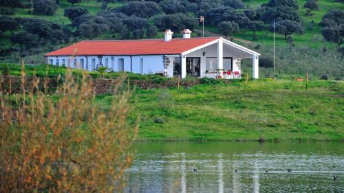 a white house with a red roof next to a lake at Casa Rural Cruces de Caminos in Plasencia