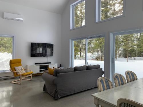 a living room with a couch and a tv and windows at Le Péribonka in LʼAscension