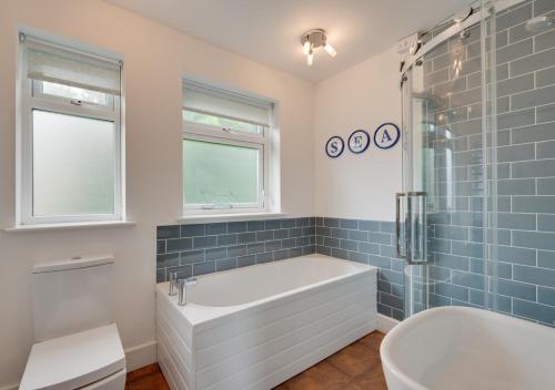 a bathroom with a tub and a shower with blue tiles at The Albatross 12 in Woolacombe
